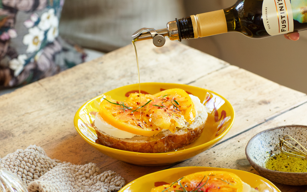 Garlic Infused Extra Virgin Olive Oil drizzled over toast with slices of fresh mozzarella and yellow heirloom tomatoes in a warm, old world kitchen setting